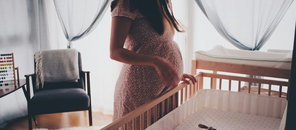 Pregnant woman standing beside a nursery crib, preparing for her baby's arrival